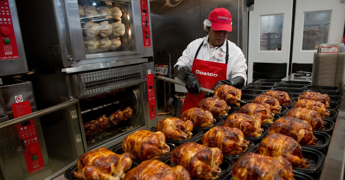 A Costco employee loading rotisserie chickens onto a rack in the warehouse deli