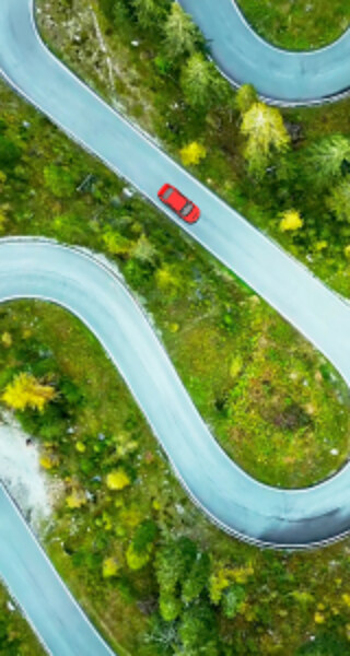 Aerial view of a red car on a winding road through green countryside