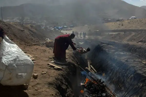 Yushu County, Qinghai Province, China: An ethnic Tibetan monk throws the body of a child onto a funeral pyre in a ditch in Jiegu Town of Yushu County, Qinghai province, after an earthquake registering 7.1 on the richter scale hit the area. April 19, 2010. Over 1,400 people died in the disaster.