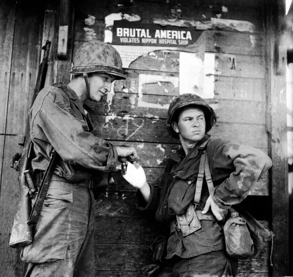 Field Dressing
              
              An American soldier stands nonchalantly while another bandages his hand during the campaign to retake the Philippines from occupying Japanese forces, Leyte, Philippines, October 1944. The pair lean against a wall which has a torn Japanese propaganda poster which reads,  Brutal America Violates Nippon Hospital Ship.