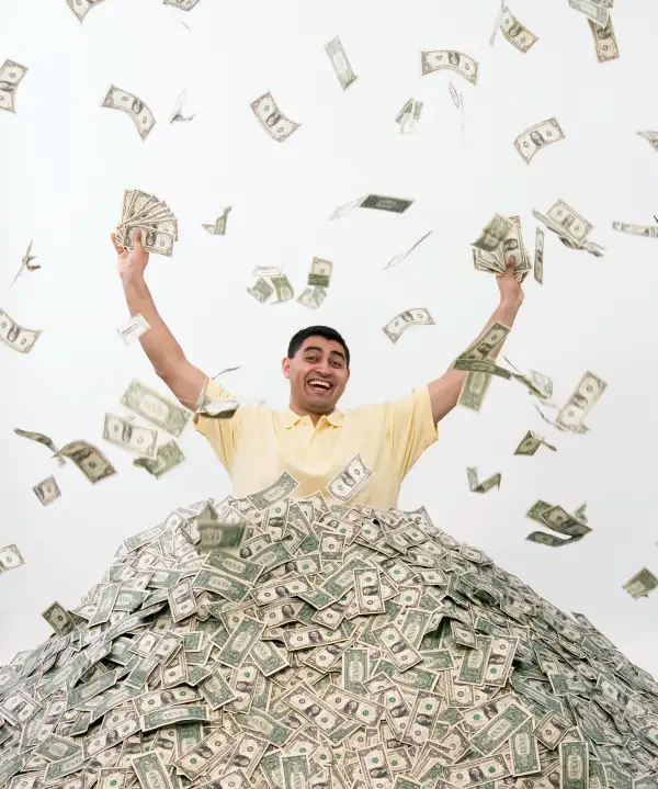 Man in pile of cash excited holding up fistfuls of money