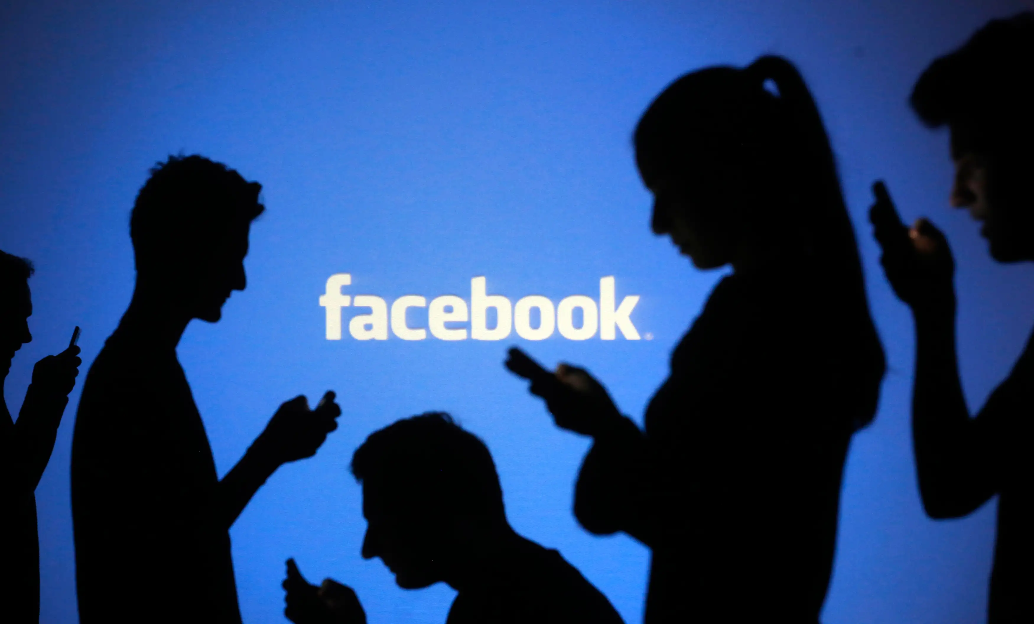 silhouettes of people using mobiles in front of FAcebook logo