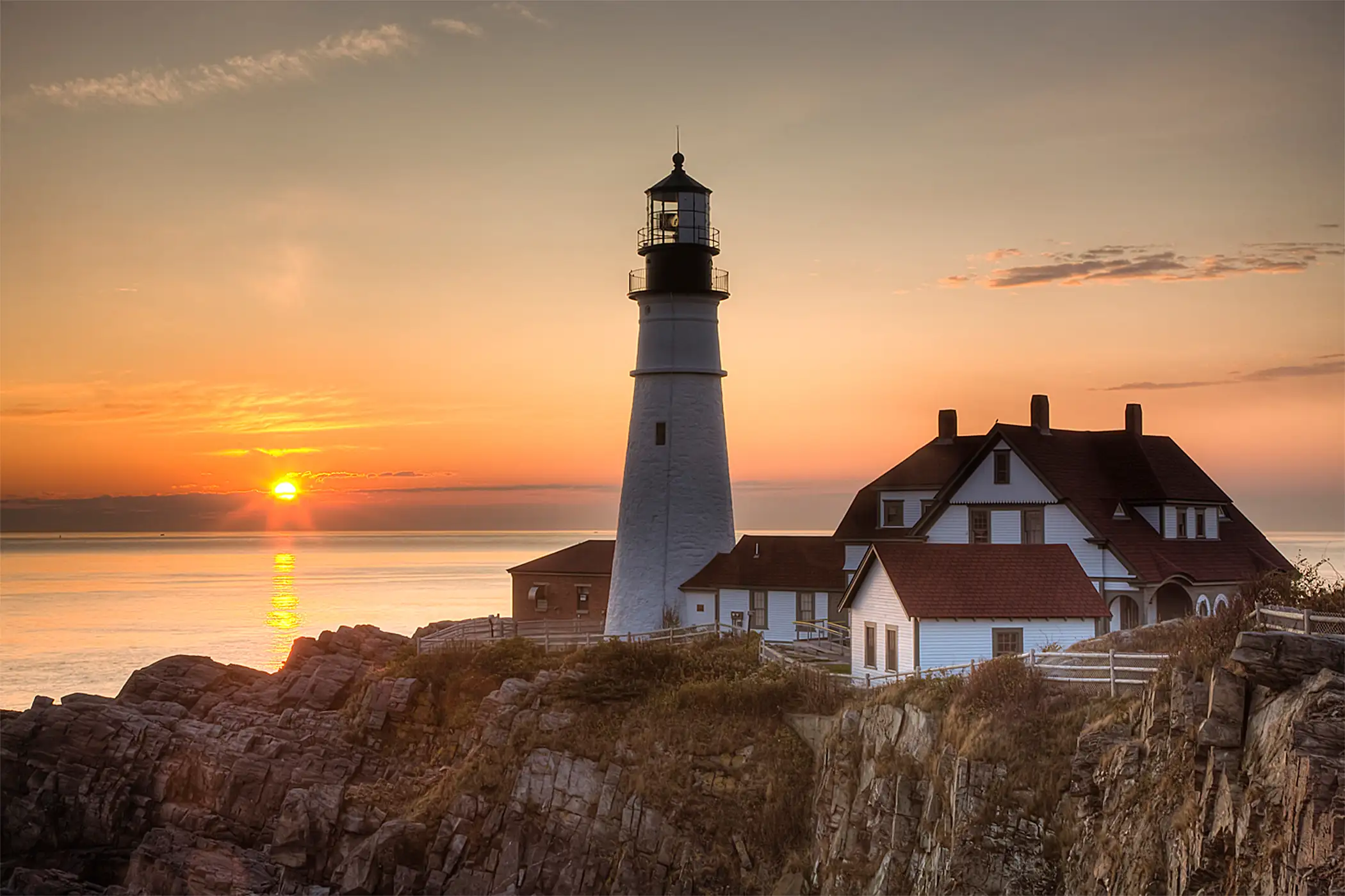 The first rays of sun after sunrise reach the Portland Head Light, built in 1791, which protects mariners entering Casco Bay. The lighthouse is located in Fort Williams Park, Cape Elizabeth, Maine, USA.