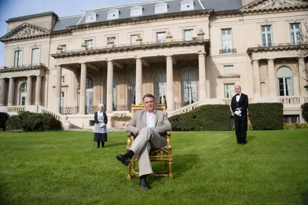 wealthy man sitting on lawn in front of mansion