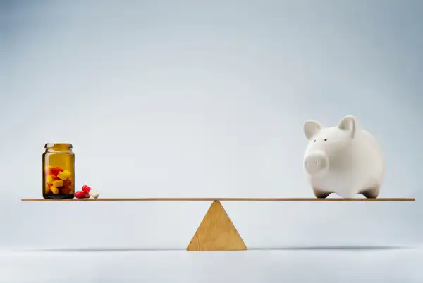 piggy bank and bottle of pills balancing on either side of a seesaw
