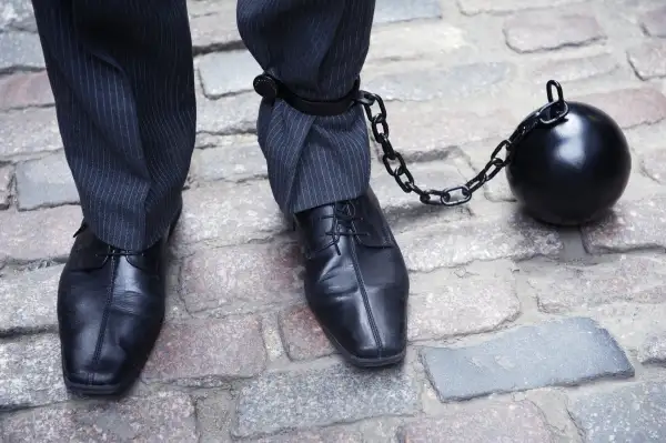 ball and chain connected to businessman's legs