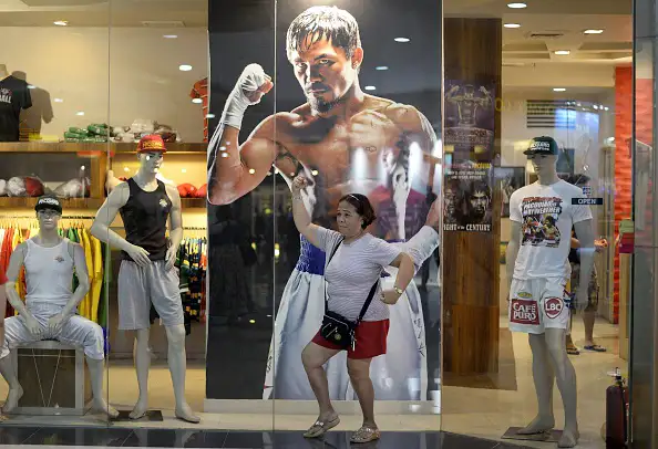 A woman poses in front of a poster of Philippine boxing icon Manny Pacquiao at a store in Manila. Manny Pacquiao's face is on shirts, dolls and postage stamps, his life story is playing in movie houses and millions are getting ready to party as the Philippine boxing hero's  fight of the century  nears.