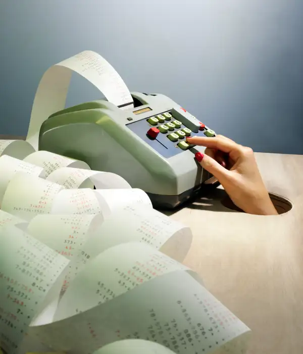 hand reaching out of hole using adding machine with rolls of paper