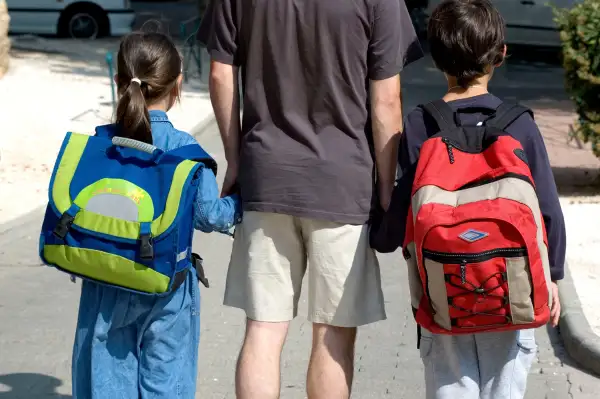 parent holding hands with two kids with backpacks