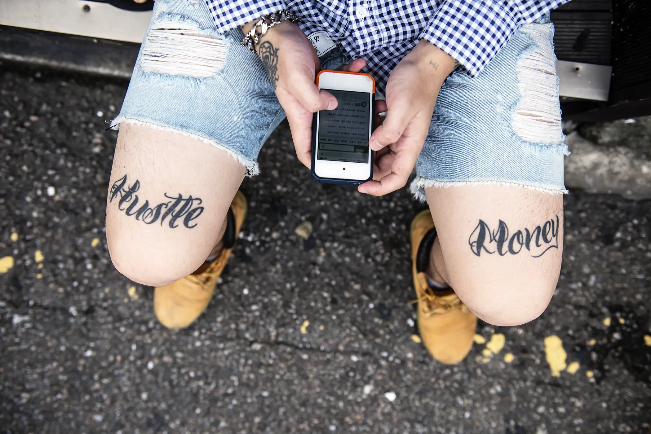 Millennial with the words  Hustle  and  Money  tattooed on each leg using his iPhone
