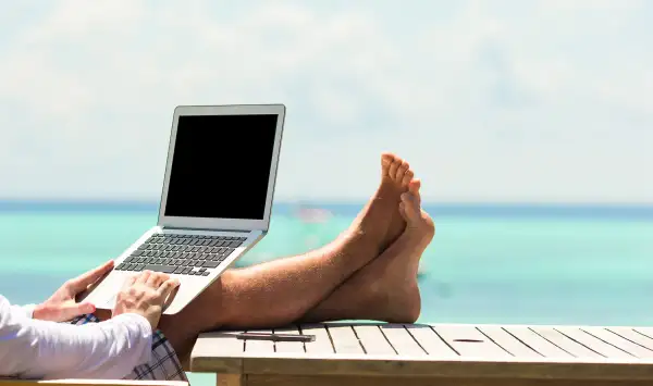 man typing on laptop with ocean view in background