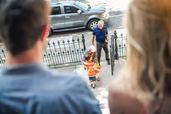 middle aged couple watching child run to grandparents outside apartment building