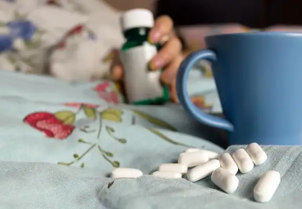 pills, medicine and mug of tea on bed blanket