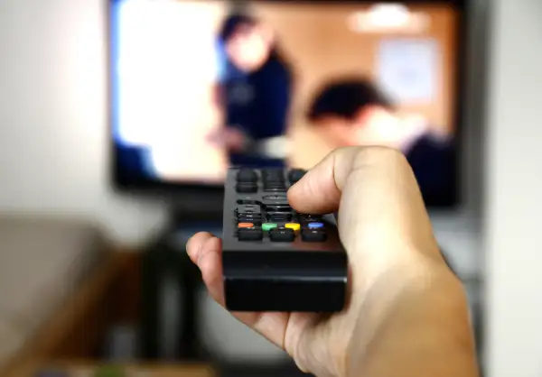 person changing channel on remote control for television set