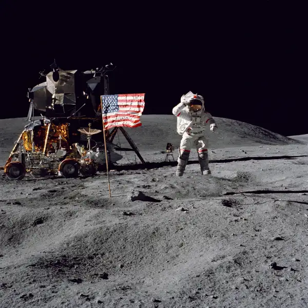 Astronaut John W. Young, commander of the Apollo 16 lunar landing mission, leaps from the lunar surface as he salutes the United States flag at the Descartes landing site near Stone Mountain during the first Apollo 16 extravehicular activity (EVA), April 16, 1972. The Lunar Module  Orion  is at the left with the Lunar Roving Vehicle is parked beside it.
