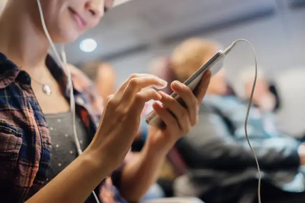 woman using smartphone and headphones on airplane