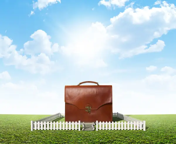 photo illustration of briefcase surrounded by picket fence on grass lawn