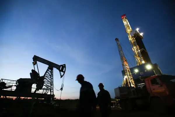 Oil workers pass a pumping unit, also known as a  nodding donkey  or pumping jack, left, at a drilling site operated by Tatneft OAO near Almetyevsk, Russia, on Friday, July 31, 2015.