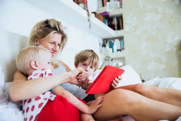 Mother with her sons watching tablet in bed