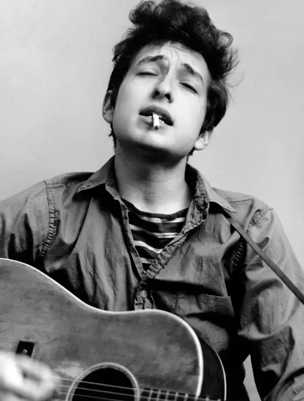 Bob Dylan plays acoustic guitar and smokes a cigarette in this headshot from September 1961 in New York City, New York.