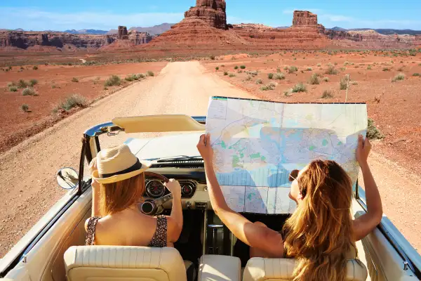 girls in convertible with roadmap in desert