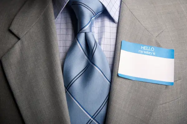 man wearing  HELLO my salary is  sticker on suit