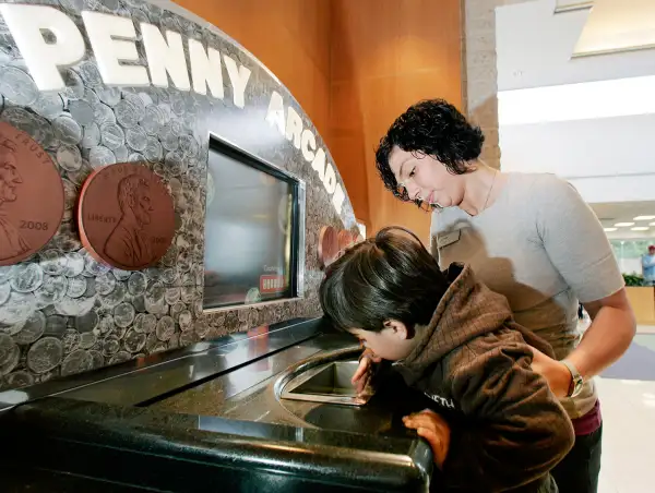 In this April 11, 2009 photo, three-year-old Charlie Cala gets help from TD Bank employee Lisa Louden as he loads his change into the bank's Penny Arcade coin counting machine at a TD Bank branch in Fairless Hills, Pa. TD Bank offers free coin turn-ins at its Penny Arcade machines, regardless of whether you're a customer.