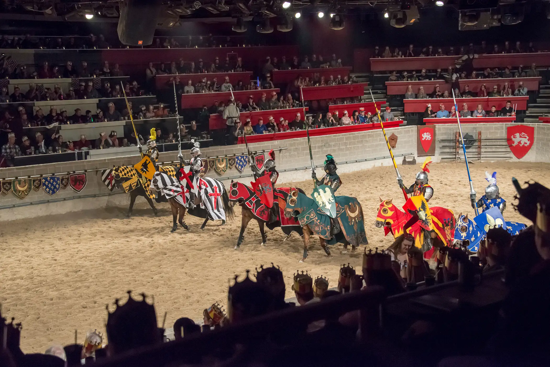 Medieval Times Restaurant: Six horsemen at a jousting event, dressed as medieval knights holding lances, lined up in a stadium full of spectators, waiting to begin the show, Toronto, Ontario, March 21, 2015.