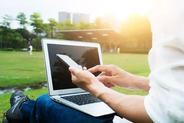 person laying on grass with laptop and cell phone