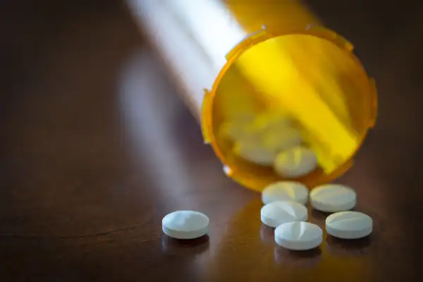 Prescription pills in a yellow bottle over a wooden table