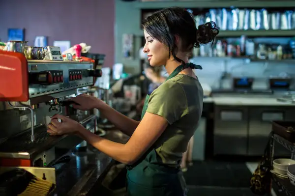 Teenage waitress preparing coffee in cafe kitchen