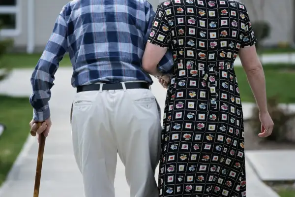 man walking with cane, being helped by woman