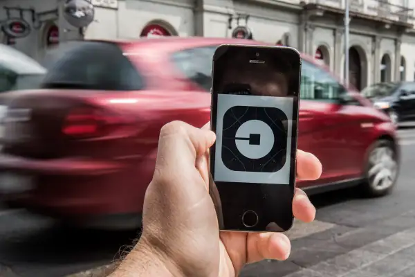 A customer holds an Apple Inc. iPhone displaying the Uber Technologies Inc. car service taxi application (app) logo as a vehicle passes by in this arranged photograph in Budapest, Hungary, on Wednesday, July 13, 2016.