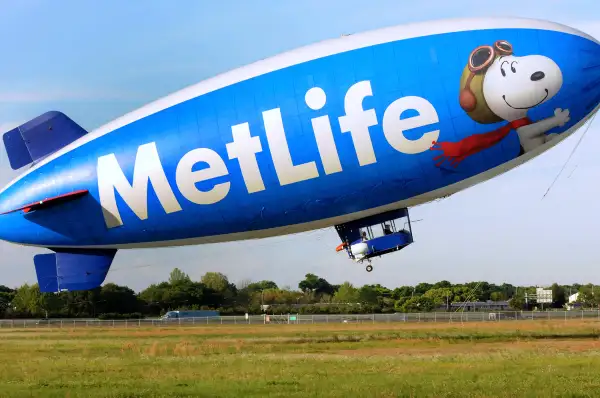 Snoopy One , a 128 foot long blimp, begins its ascent for an excursion at the Orlando Executive Airport, March 28, 2015, in Orlando, Florida. The airship was first launched in February 1994 and is one of two brand ambassadors for the Metropolitan Life Insurance Company (MetLife) in the United States. The helium-filled blimp is one of 12 airships owned and operated by the Van Wagner Airship Group. Snoopy One bears the MetLife logo as well as images of the Peanuts comic strip characters, Charlie Brown and Snoopy, and an advertisement for the Peanuts Movie, a computer-animated 3D film scheduled for release in November 2015. The blimp flies five days a week providing television coverage of sporting events, doing flyovers, and making special appearances.