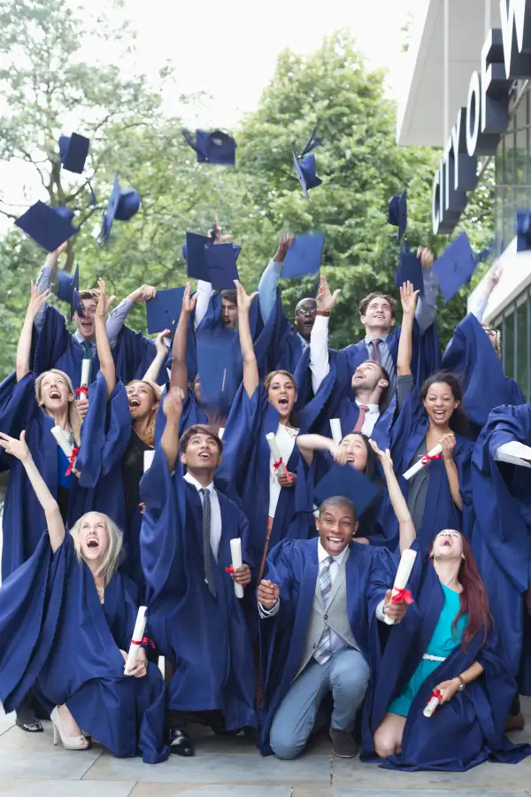 Group portrait of students in graduation gowns throwing mortarboards in the air