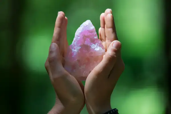 Hands holding healing crystal on green.