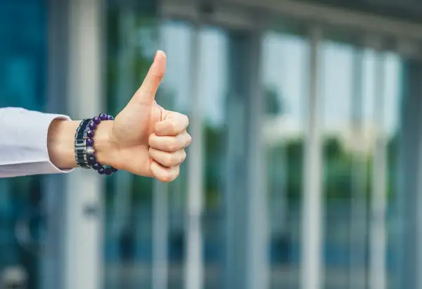 Hand with thumbs up in front of a modern building.