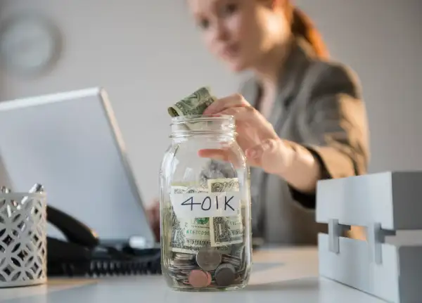 Businesswoman putting money into 401K jar at desk