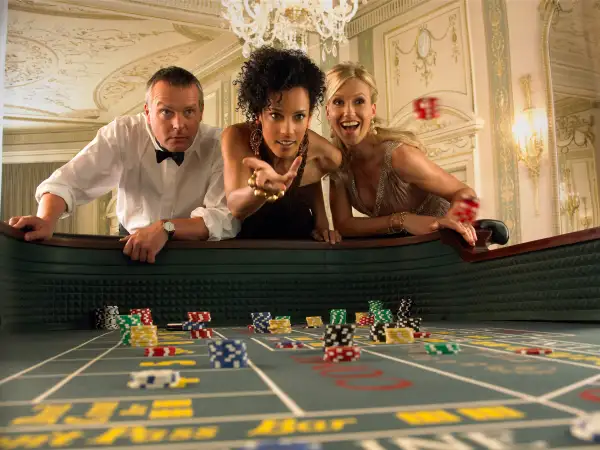 Woman throwing dice at craps table in casino, friends watching