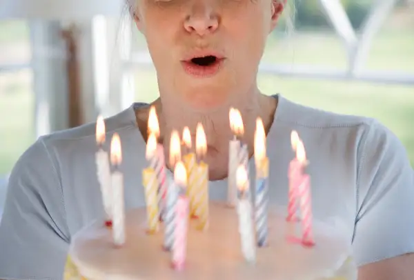 Senior woman holding up birthday cake with lit candles.