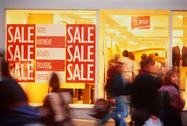 Shoppers entering store with sale signs displayed in window