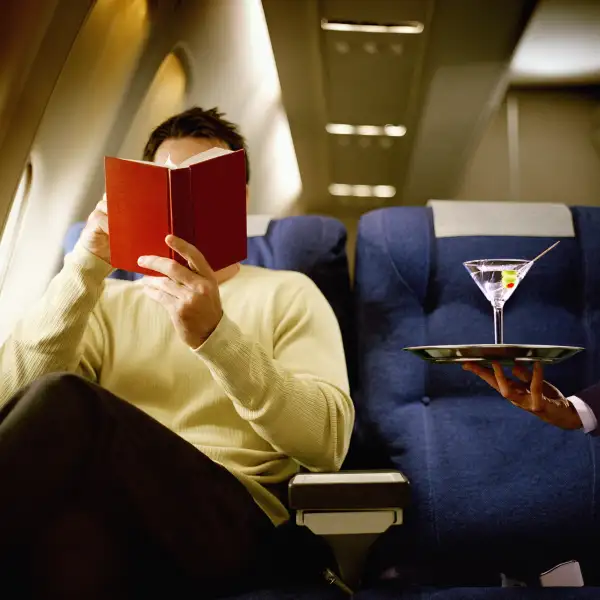 Man reading book, being served martini, in first class on airliner