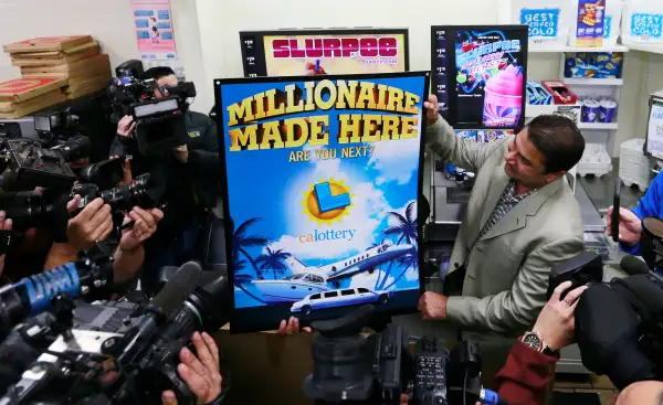 7-Eleven franchise owner Balbir Atwal, right, who will receive $1 million for selling a winning ticket, holds a Powerball poster as media crowds around at Chino Hills store, January 14, 2016.