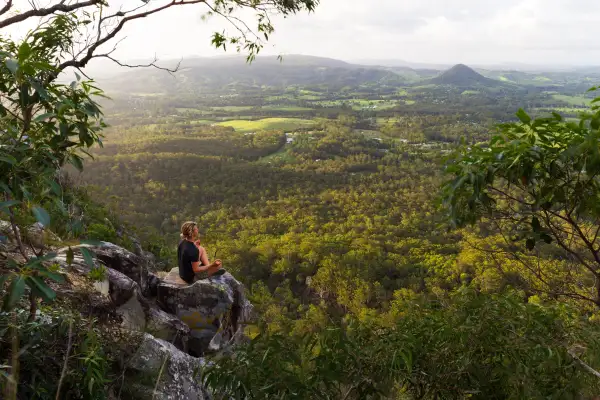 A young man meditates on top of a mountain with expansive views near Noosa Heads, Australia.