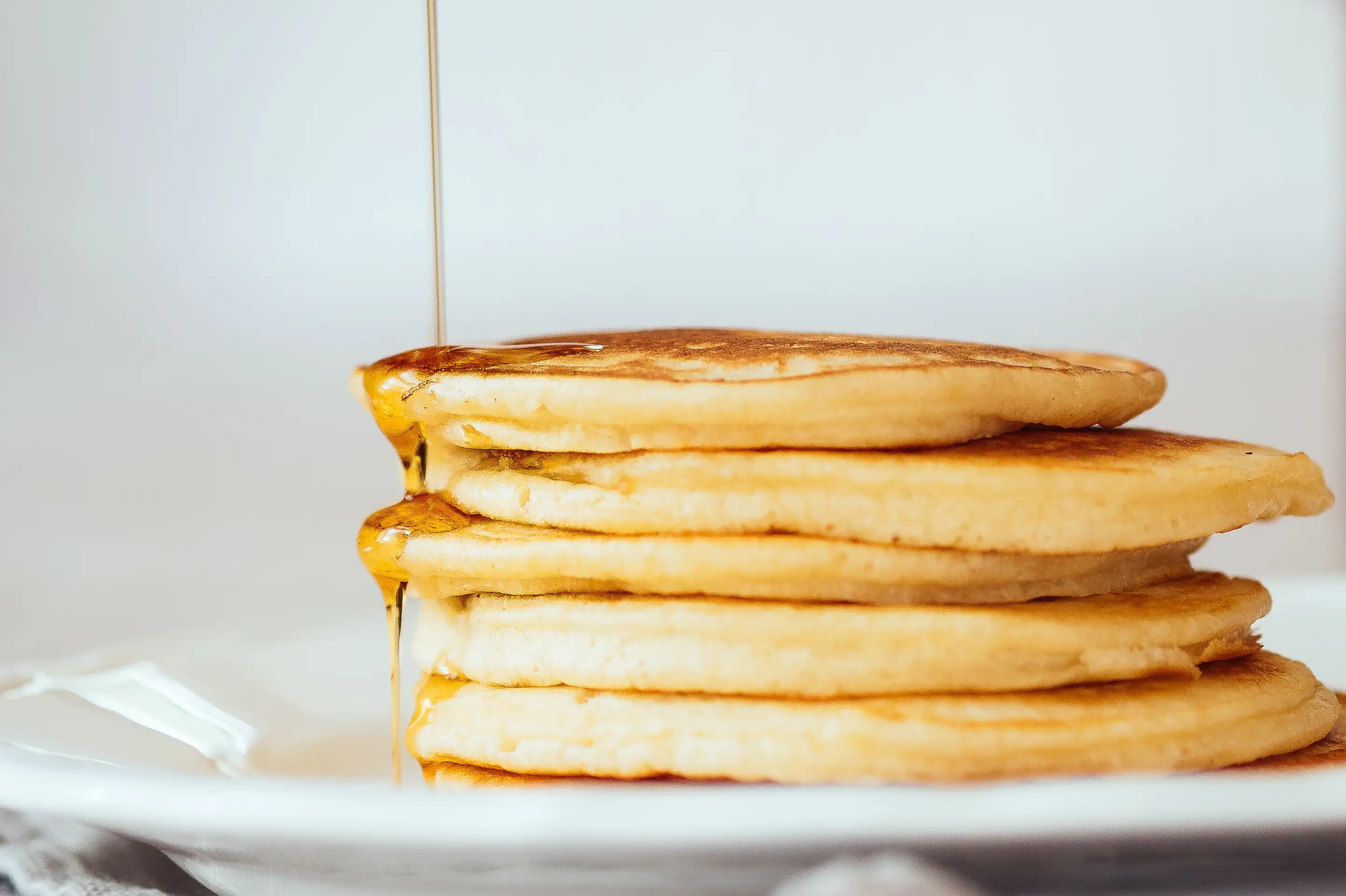 Maple Syrup Falling On Pancakes Served In Plate On Table