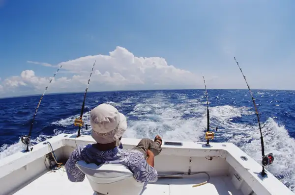 Man in chair fishing from deck of boat, rear view (wide angle)