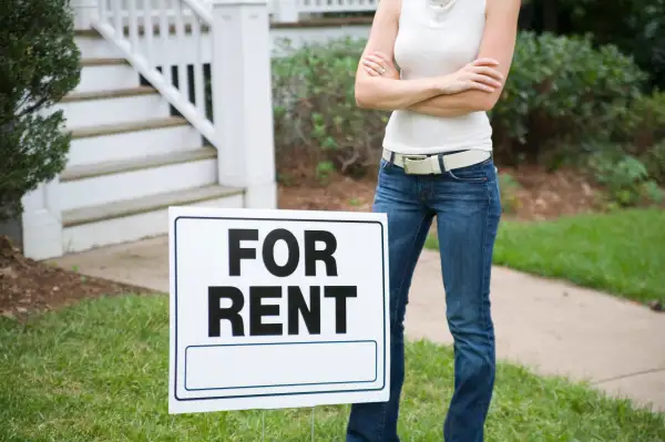 A young woman standing behind a ?for rent? sign