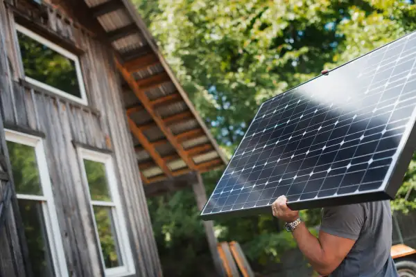 A man carrying a solar panel on a green construction site, working on a green building project.