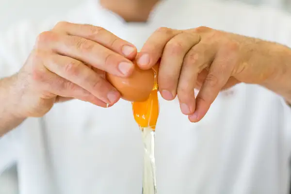 Close-Up Of Hand Breaking Egg