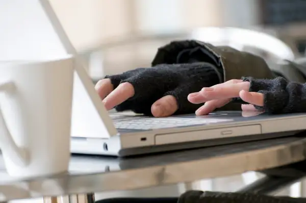 young male using laptop computer keyboard wearing fingerless gloves